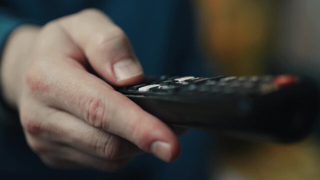 Close up of a hand clicking buttons on a TV remote control to change channels.