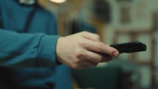 Close up of a hand clicking buttons on a TV remote control to change channels.