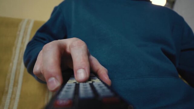 Close up of a hand clicking buttons on a TV remote control to change channels.