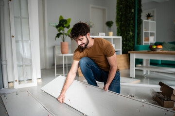 Obraz premium Young man assembling flat pack furniture for home improvement