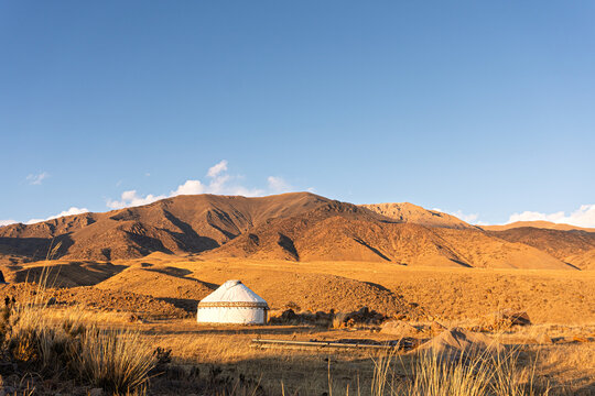 Traditional white yurt in a mountain valley during golden hour. Scenic landscape of a nomadic dwelling in Central Asia(Kyrgyzstan). Copy space