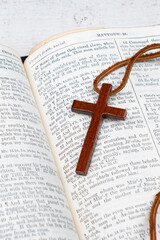 A wooden cross necklace on an open Bible with a shallow depth of field
