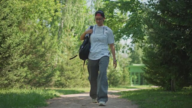 smiling man looking up on sunlit path with shoulder bag, joyful gaze through leafy canopy, slow confident walk, leaves dappling light on face, refreshing breeze, serene summer moment
