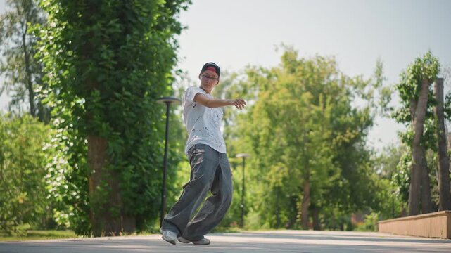 asian man shuffling dance in park, sunlit pathway and green trees, street dancer rehearses precise footwork and balance, tests new choreography and rhythm, wears cap and casual outfit, focused