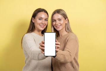 Fototapeta premium Two happy young women friends showing a smartphone with a blank white screen