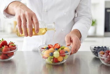Professional chef pouring dressing over a fresh fruit salad in a glass bowl in a kitchen
