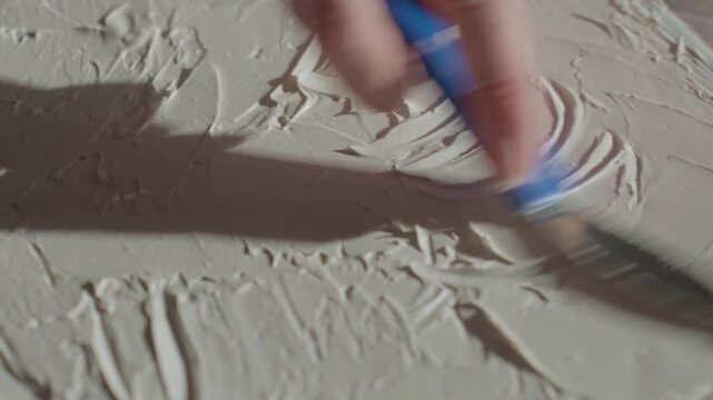 Close up of woman creating textured relief on canvas using palette knife and thick paste