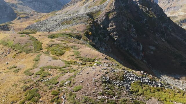 Rugged mountains stretch under golden sunlight. Slopes show wild grasses, rocks, and patches of green. No people are visible in this remote landscape