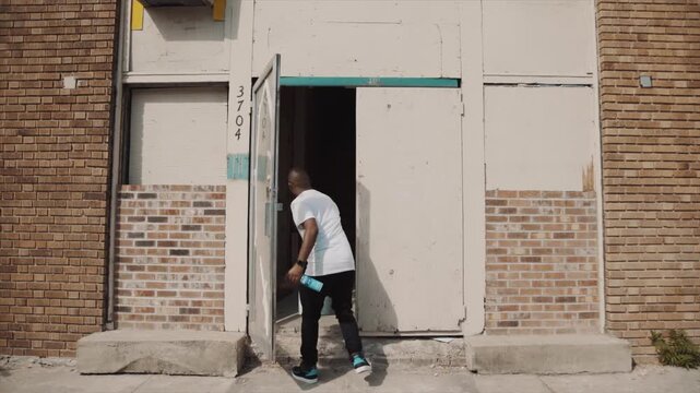 African American man carrying a paint bucket walking into a derelict urban building entrance