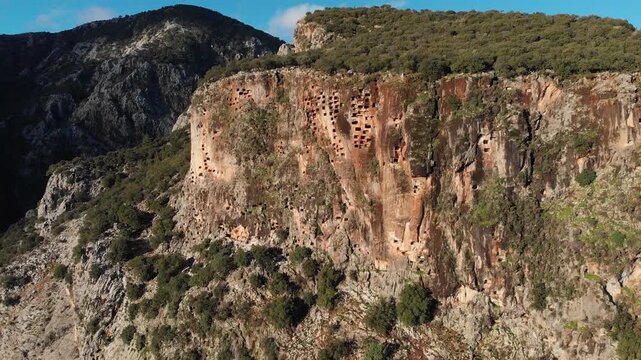 Drone slowly flying over  Telmessos Ancient City ruins nestled in a lush green mountain forest in Turkey, ab01