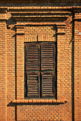 Classic rectangular window set in a rich red brick wall, featuring thick decorative brick lintel, with dark weathered wooden shutters © Bits and Splits