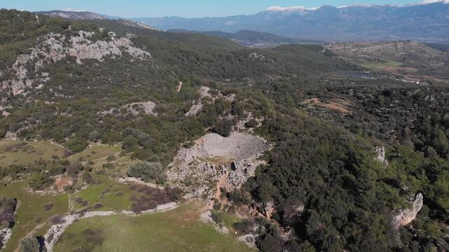 Drone slowly flying over  Telmessos Ancient City ruins nestled in a lush green mountain forest in Turkey, ab01