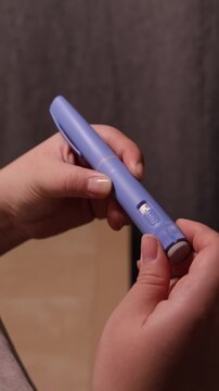 A vertical close up of a young woman priming the pen injector with semaglutide, prepering it for injection
