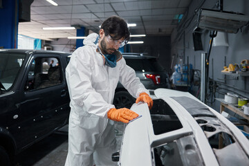 Automotive technician sanding car body panel with orange gloves and protective coverall