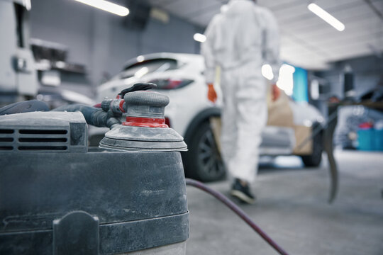 Auto body shop car painting prep with orbital sander and technician in protective suit