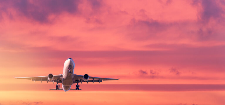 Commercial passenger airplane taking off. Aircraft flying up into dramatic pink and orange cloudy sky at sunrise. Air transportation and travel concept and background. Business trip