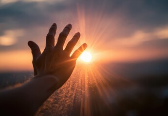 Hand reaching out towards the vibrant setting sun with a beautiful sky.