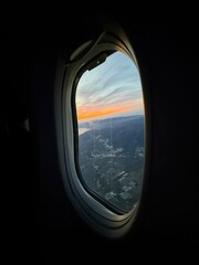 Fototapeta premium View from an airplane window during sunset, warm golden light reflecting on the aircraft wing, dramatic clouds and colorful sky, high-resolution travel photography.