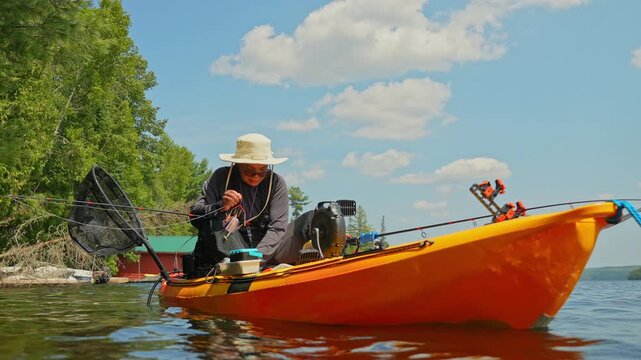 Woman setting up her tackles lure or bait to the braid line while slowly floating on water waves. Kayak sport fishing. Tourist enjoys kayak fishing at scenic coastline. Peaceful water setting at lake.