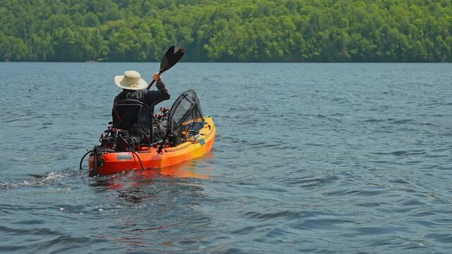 Woman paddling on kayak boat slow motion. Kayaking lake with scenic landscape. Woman angler in a sun hat on motorized kayak enjoying peaceful summer vacation sunny day while active outdoor.