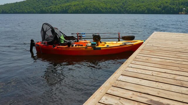 Fully rigged kayak watercraft mooring and tied to boat pier near cottage. Kayaking lake during tournament or fishing derby. Kayak water craft equipment for fishing activities. Recreational watercraft.