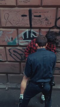 Law enforcement officers isolate and hold suspect against graffiticovered brick wall in narrow alley