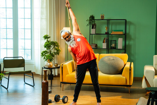 Bearded Indian man performing mobility workout with staff or stick indoors at home