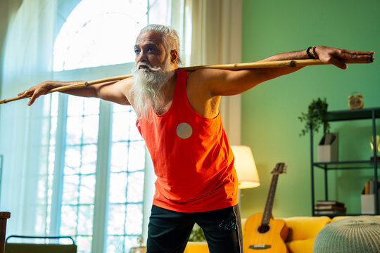 Bearded Indian man performing mobility workout with staff or stick indoors at home
