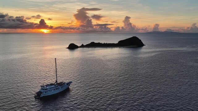 A serene sunrise silhouettes a small island in the Vatu-i-ra seascape in Fiji. This area is a marine protected area known for its high biodiversity and is a destination for divers and snorkelers.