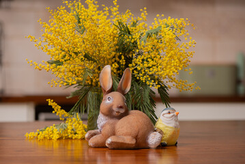 Easter bunny figurine with tit bird and mimosa bouquet, spring holiday decoration in the modern kitchen interior. Cozy spring composition good for Easter celebration and seasonal decor. © Hanna Aibetova