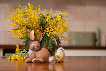 Easter bunny figurine with tit bird and mimosa bouquet, spring holiday decoration in the modern kitchen interior. Cozy spring composition good for Easter celebration and seasonal decor. © Hanna Aibetova