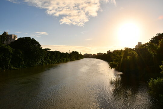 Paisagem fluvial urbana ao p&ocirc;r do sol com mata ciliar e silhueta de pr&eacute;dios