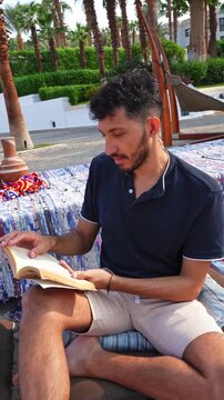 Man Reading a Book While Relaxing Outdoors in Tropical Resort Setting