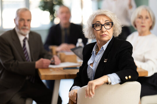 During meeting, girl with remote controller tell material, speaks to mature precursors of business group. Staff or co-founder during discussion of companys development strategy