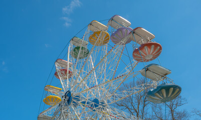 Colorful Ferris wheel with multi-colored cabins stands against a bright blue sky, capturing the nostalgic and joyful atmosphere of a classic amusement park © John_Doo78