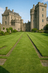 Fototapeta premium Historic stone castle with tall towers and a wide green lawn leading to the entrance under clear daylight showcasing medieval architecture heritage travel charm and timeless grandeur