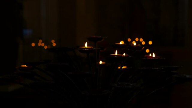 Votive candles burning with flickering flames in a dark church. Numerous small votive candles burning brightly on a metal stand inside a dark and tranquil religious sanctuary