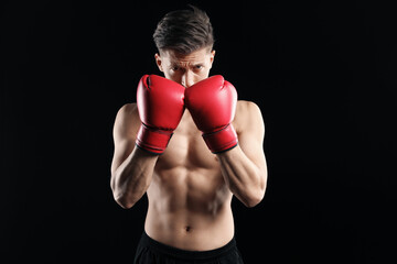 Athletic man in red boxing gloves on black background