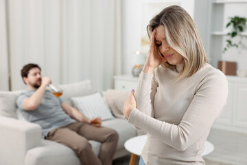 Alcohol addiction. Drunk man with whiskey on sofa at home, focus on his unhappy wife