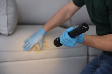Man with flashlight looking at stain on sofa, closeup