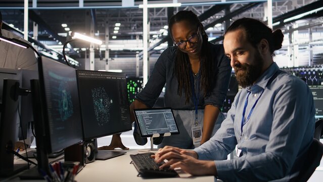 Data center system administrators working together, collaborating on neural network software development. Server hub worker and african american colleague implementing AI tech in workplace, camera A