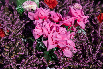 Pink artificial roses and purple heather floral tribute outdoors