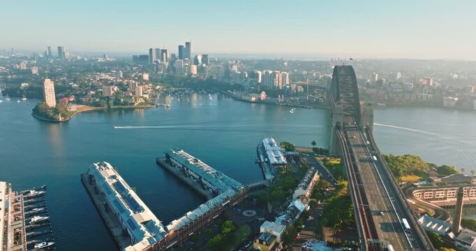 Sydney Harbour Bridge spanning across the harbor with city skyline buildings, ferry boats, and Darling Harbour waterfront visible under clear sky during daytime Aerial drone flight panorama. Australia
