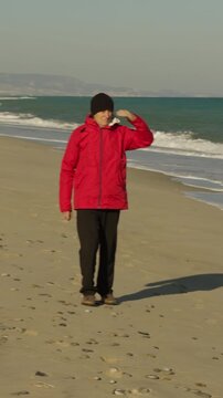Elderly man walking relaxing on the beach near the ocean with red jacket