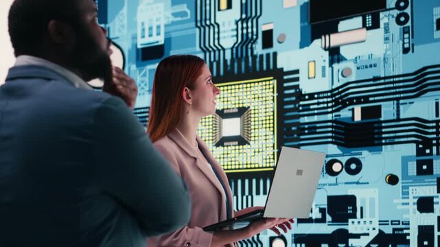 Engineering team analyzing semiconductor fabrication with laptop, looking at display. Teamworking PCB factory colleagues oversee microprocessor production with notebook, camera B