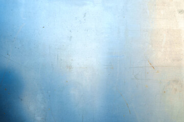 Obraz premium A horizontal close-up of a light blue metal sheet with visible scratches, small rust spots, and a bright light reflection on the surface.
