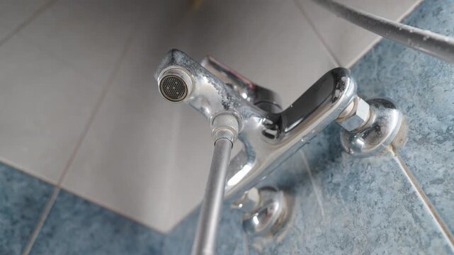 Close-Up Bottom-Up View: Dripping Water from Old Chrome Bathroom Faucet | Leaking Mixer Tap Needs Repair | Water Waste and Plumbing Problem Concept