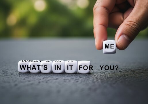 A hand places a cube with the word me onto a line of cubes spelling whats in it for you, representing selfinterest and personal gain in relationships or negotiations