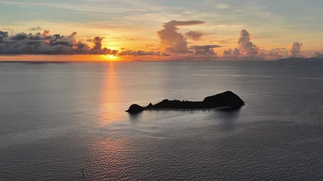 A serene sunrise silhouettes a small island in the Vatu-i-ra seascape in Fiji. This area is a marine protected area known for its high biodiversity and is a destination for divers and snorkelers.