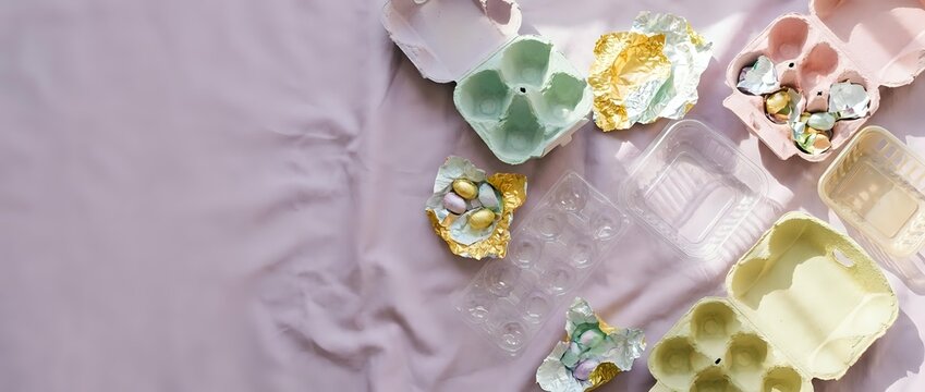 Colorful egg cartons and Easter decorations arranged on soft pink fabric background for spring holiday crafts and seasonal celebration projects.